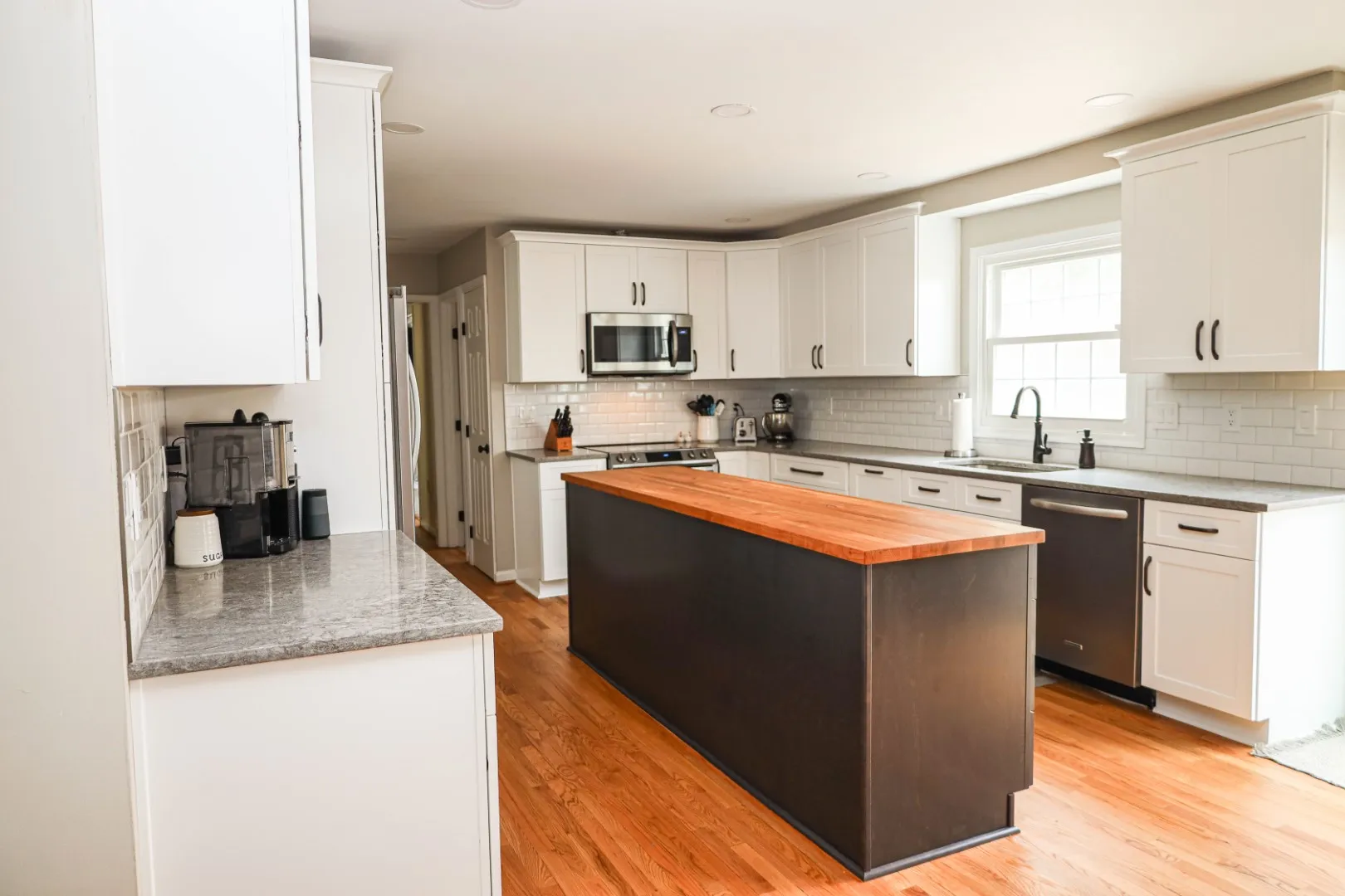 Complete kitchen remodeling in Ellicott City MD featuring classic white cabinets, a wood-top island, and hardwood floors by Anka Design Studio.