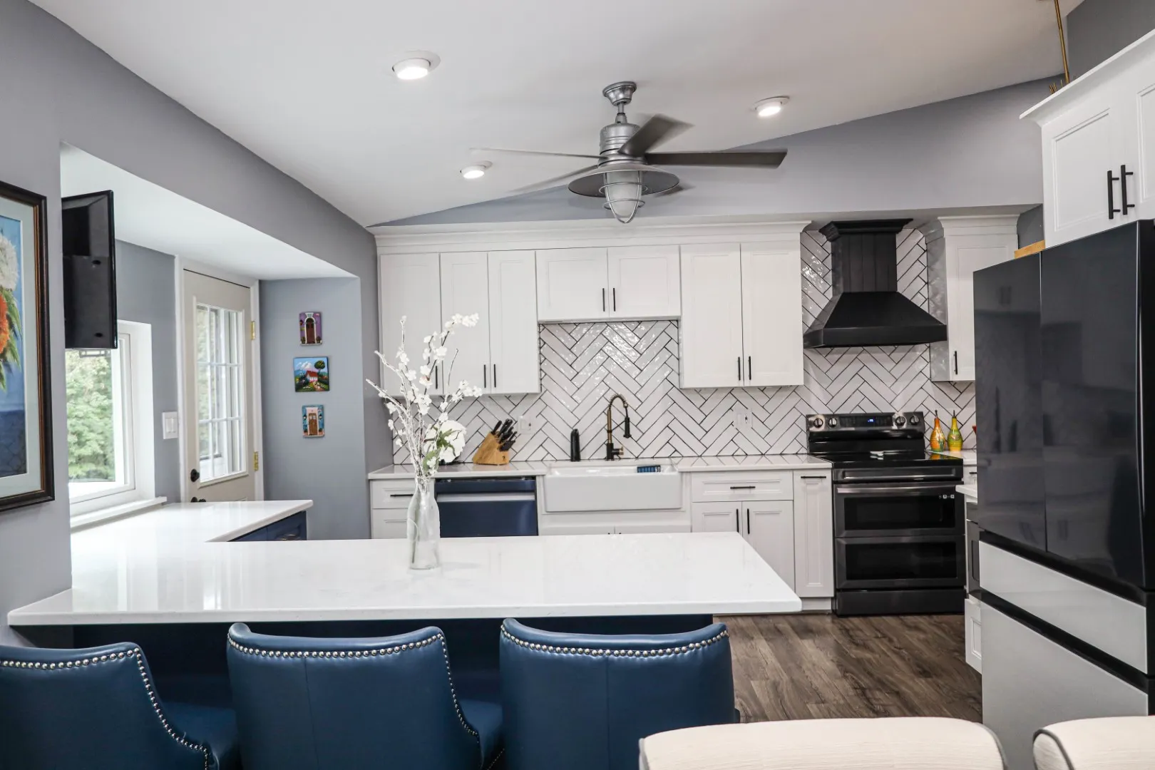 A closer view of the large kitchen island with its dark butcher block top, showing the seating area with two natural wood and metal bar stools in a newly renovated Columbia, MD kitchen. The background features white shaker cabinets and a subway tile backsplash.