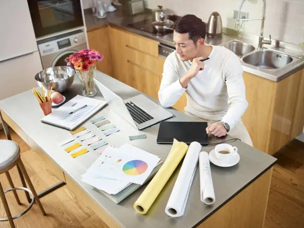 Homeowner planning a home renovation at a kitchen table with notebook, material samples and laptop showing design plans