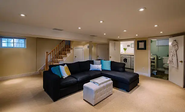 Finished basement with warm lighting, sectional sofa, and built-in shelving
